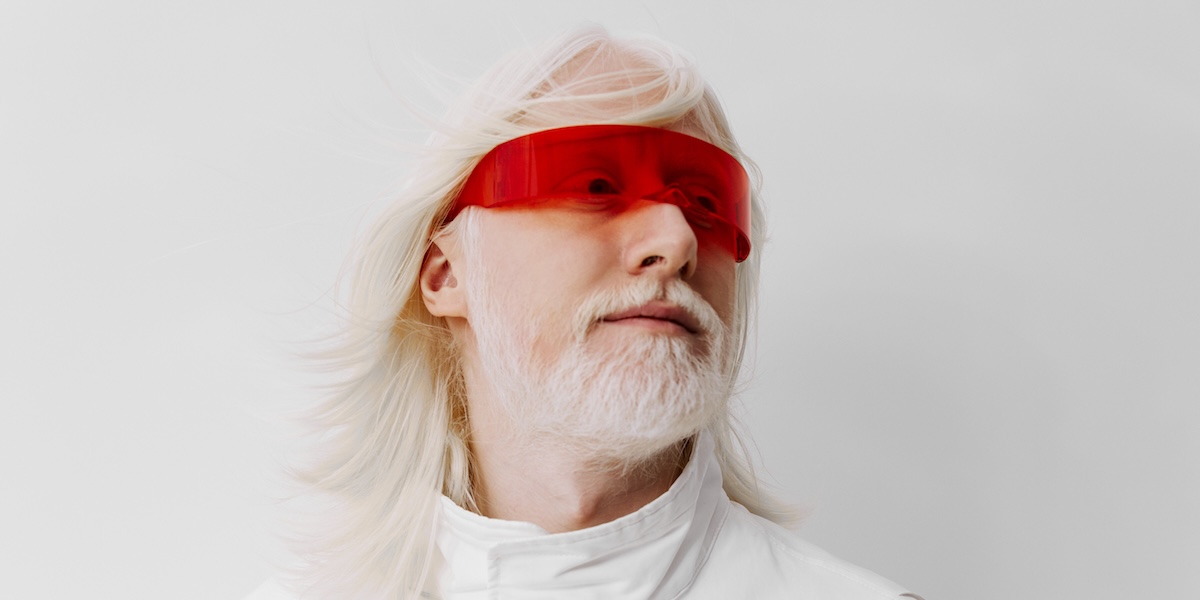 Futuristic man with white hair and red glasses, wearing a white outfit against a plain white background, showcasing a sci fi aesthetic and modern style